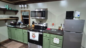A kitchen with green cabinets, a stainless steel refrigerator, a microwave, and a stove. - Owl's Nest, a rustic tiny house located 3.5 miles off I-65 in Evergreen, Alabama (Evergreen)