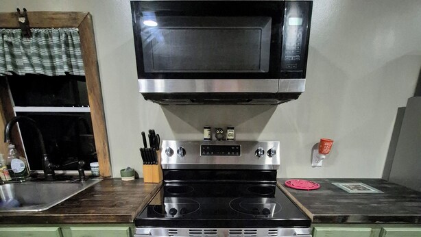 A kitchen with a stainless steel stove, a microwave above it, and green cabinets. - Owl's Nest, a rustic tiny house located 3.5 miles off I-65 in Evergreen, Alabama (Evergreen)
