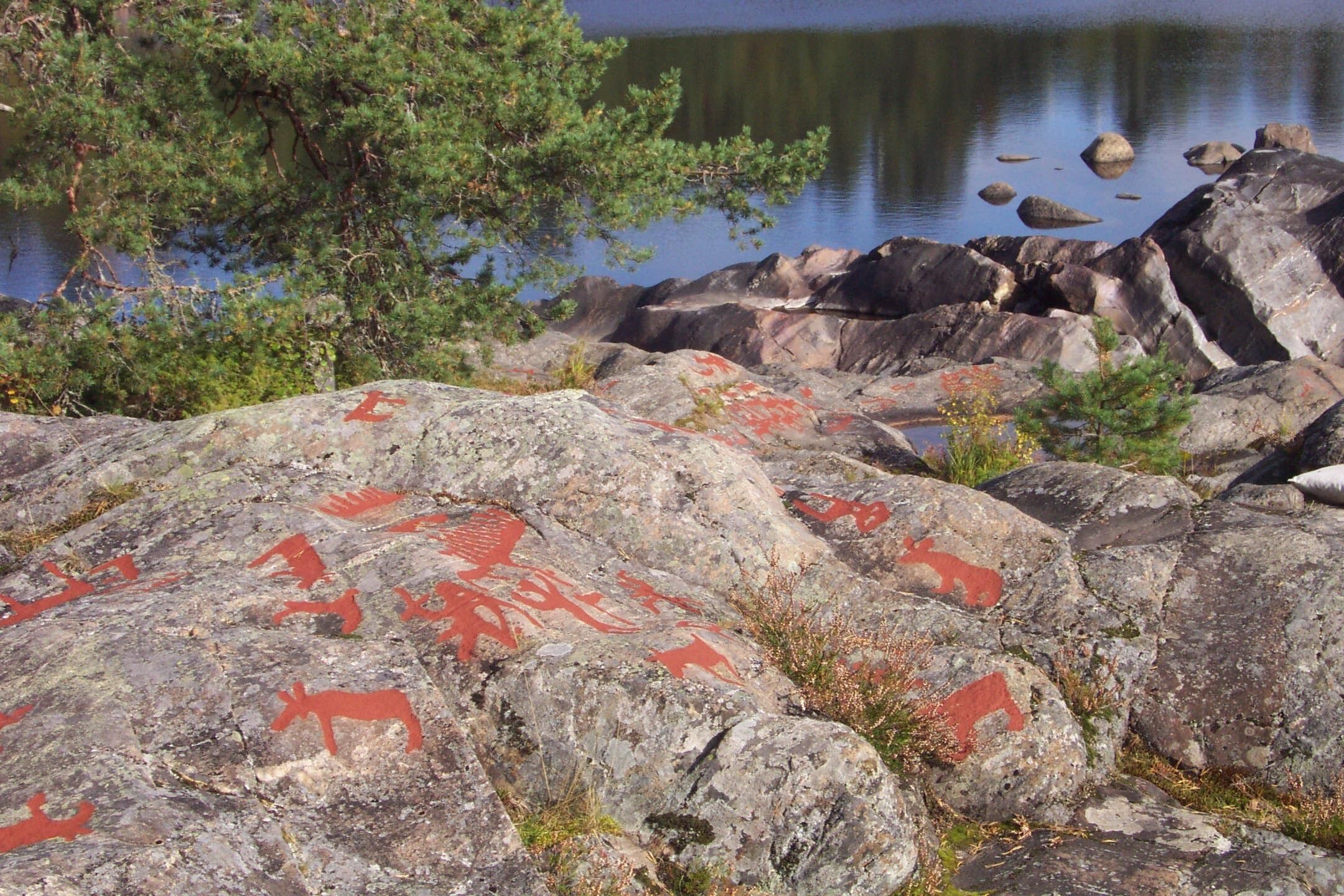 Un rivage rocheux parsemé d’empreintes d’animaux rouges, avec un lac paisible en arrière-plan.