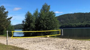 Una rete da pallavolo sulla spiaggia, con un lago e una foresta sullo sfondo.