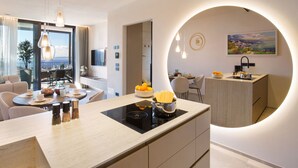 A modern kitchen with a central island, a dining area with a view, and a living space with a sofa and dining table.