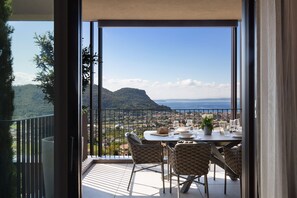 A balcony with a table set for dining, overlooking a scenic view of a coastal town and mountains. - Apartment Luna in Residence Villa Miralago (Costermano)