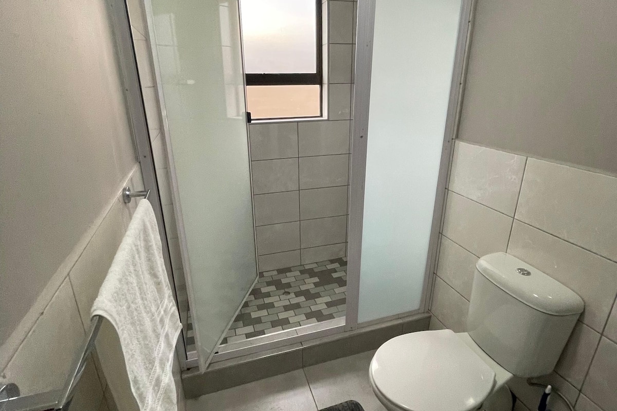Un baño con ducha, inodoro y un ventanal pequeño.