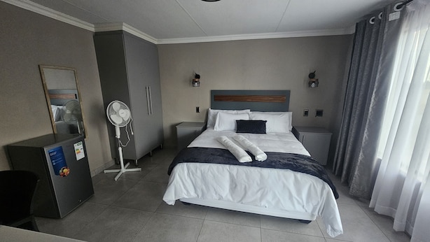 Ein Hotelzimmer mit einem Bett, Nachttischen, einem Schreibtisch, einem Ventilator und einer Minibar.