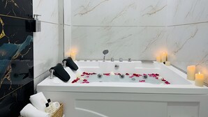 Ett modernt badrum med en vägg av marmor, ett badkar fyllt med rosenblad, ljus och hygienartiklar.