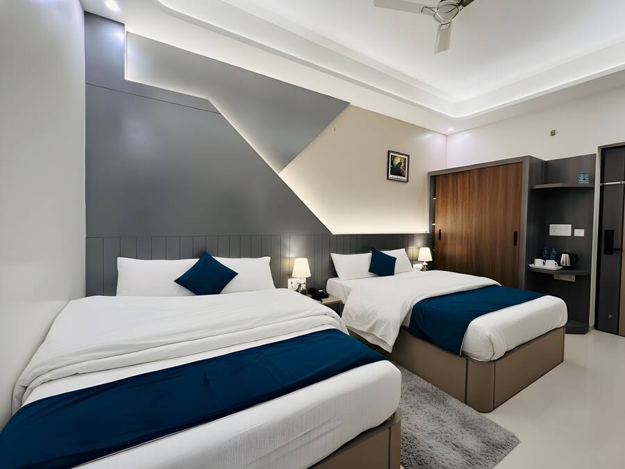 Une chambre d’hôtel moderne avec deux lits, un ventilateur de plafond, une armoire en bois et une petite table de chevet avec une lampe.