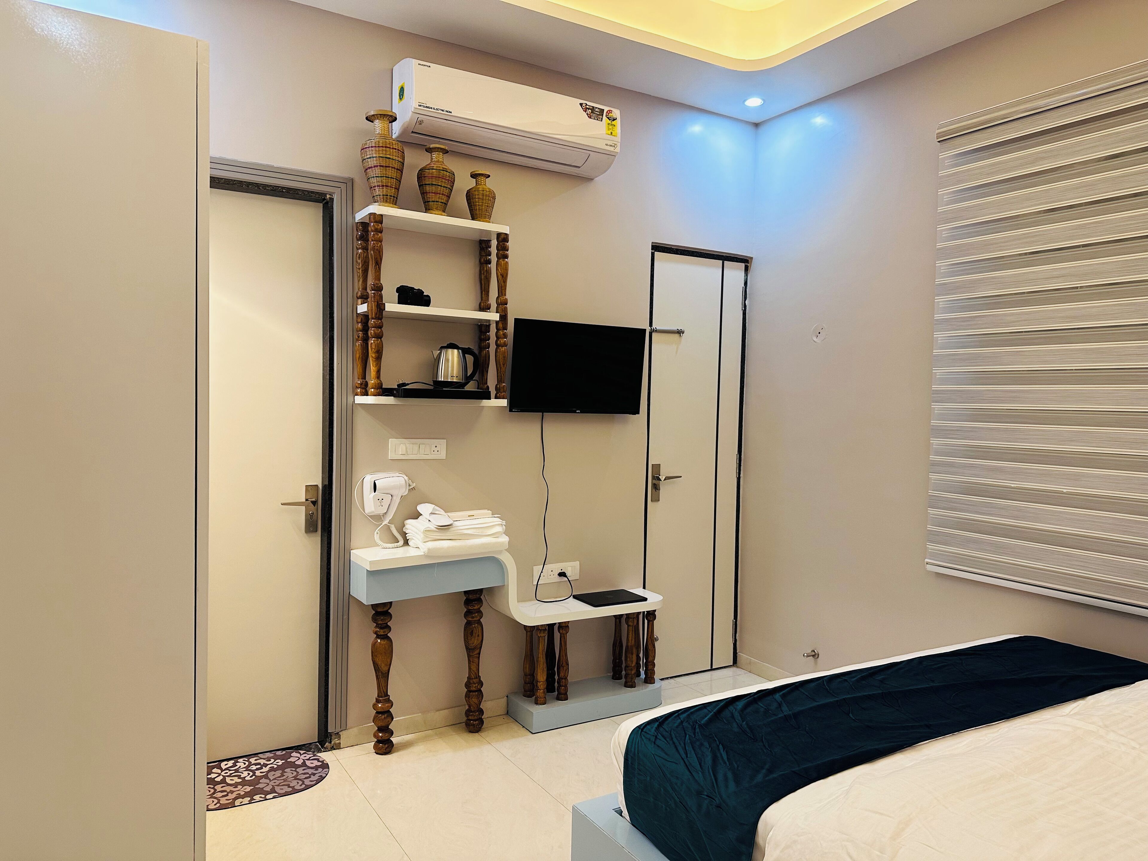 A bedroom with a bed, a vanity with a mirror, a television mounted on the wall, and a window with blinds.