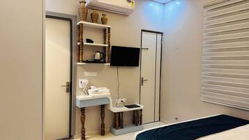 Un dormitorio con cama, tocador con espejo, televisor montado en la pared y ventana con persianas.