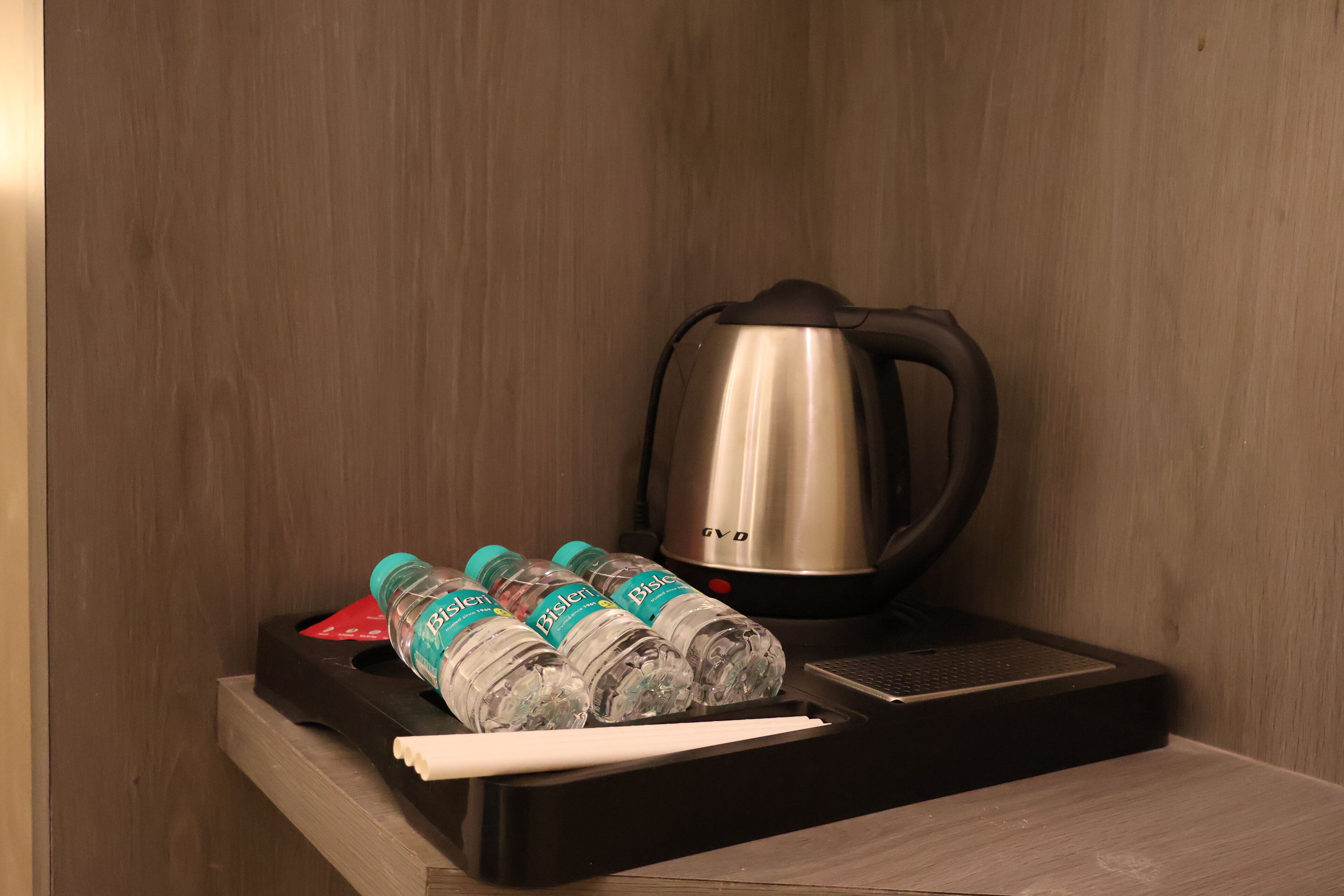 A kitchenette with a stainless steel kettle, a tray with water bottles, and a white napkin.