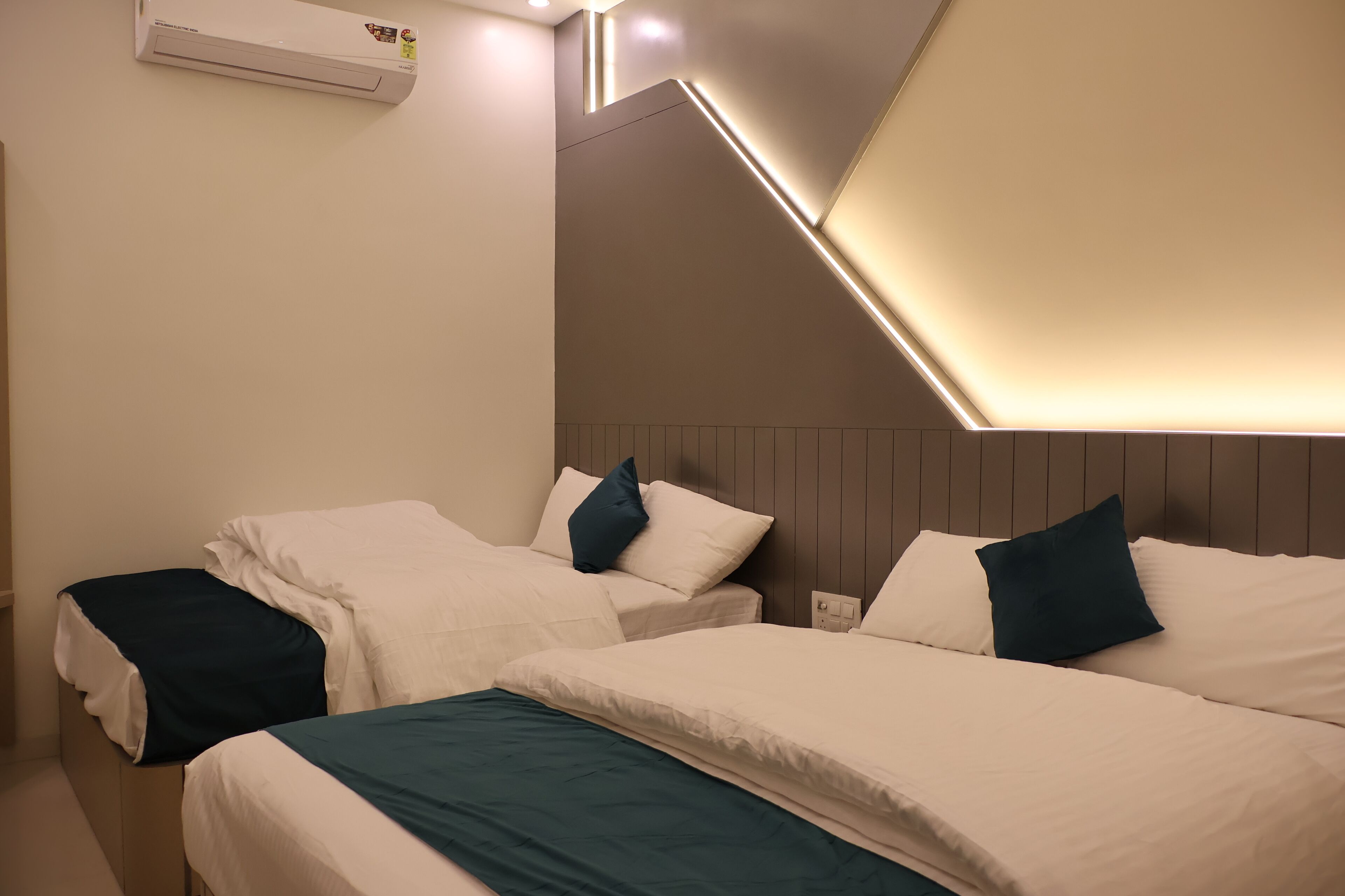 Ein Hotelzimmer mit zwei Betten, einer Decken-Klimaanlage und einer schrägen Decke mit eingelassener Beleuchtung.