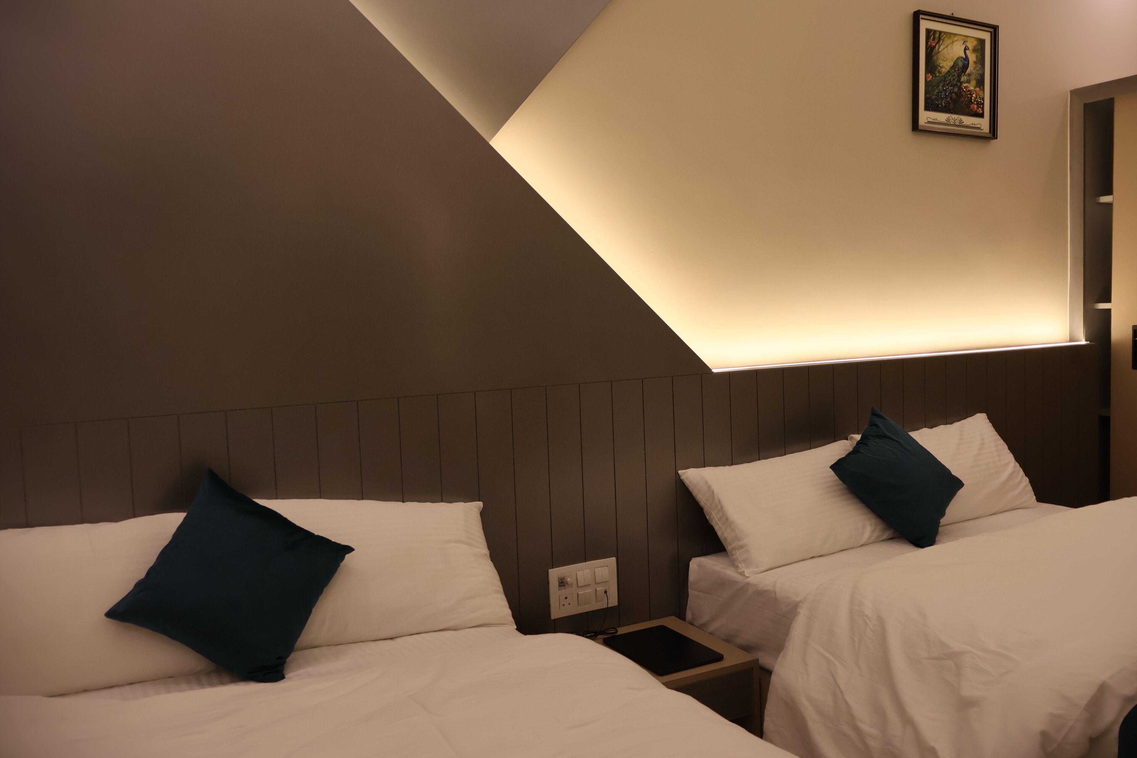 A hotel room with two beds, each with a pillow, a bedside table with a phone, and a wall-mounted light fixture.