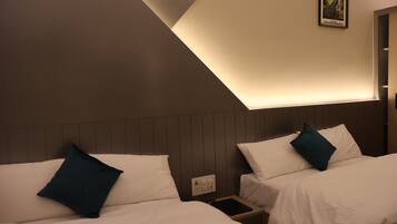 A hotel room with two beds, each with a pillow, a bedside table with a phone, and a wall-mounted light fixture.