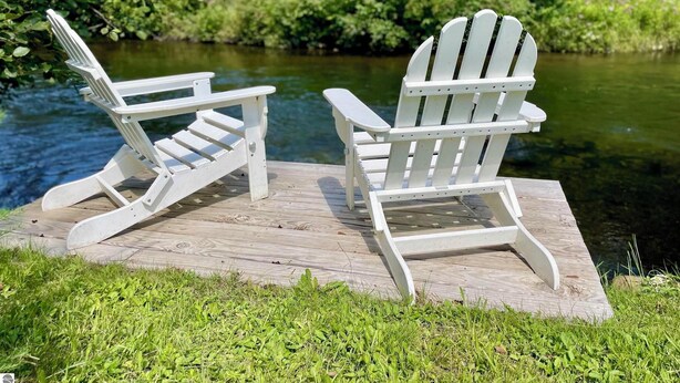 Duas cadeiras Adirondack num deck de madeira junto a um rio.