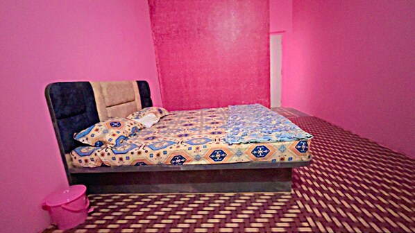 A bed with a patterned bedspread, a headboard, and a pink wall.