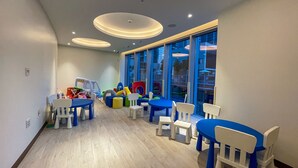 A children's play area with tables and chairs, toys, and a large window with a view.