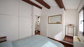 Ein Schlafzimmer mit einem Bett, Holzboden, einem Spiegel, einer Heizung und einer Treppe.