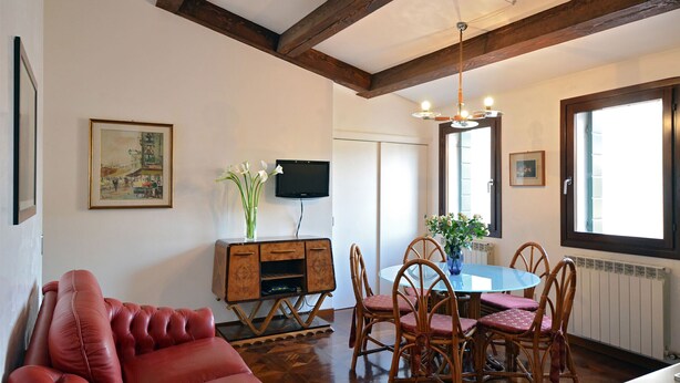 Ein Wohnzimmer mit einem roten Sofa, einem Holzespeisetisch mit Stühlen, einem Fernseher auf einer Holzkommode und einem Bild an der Wand.