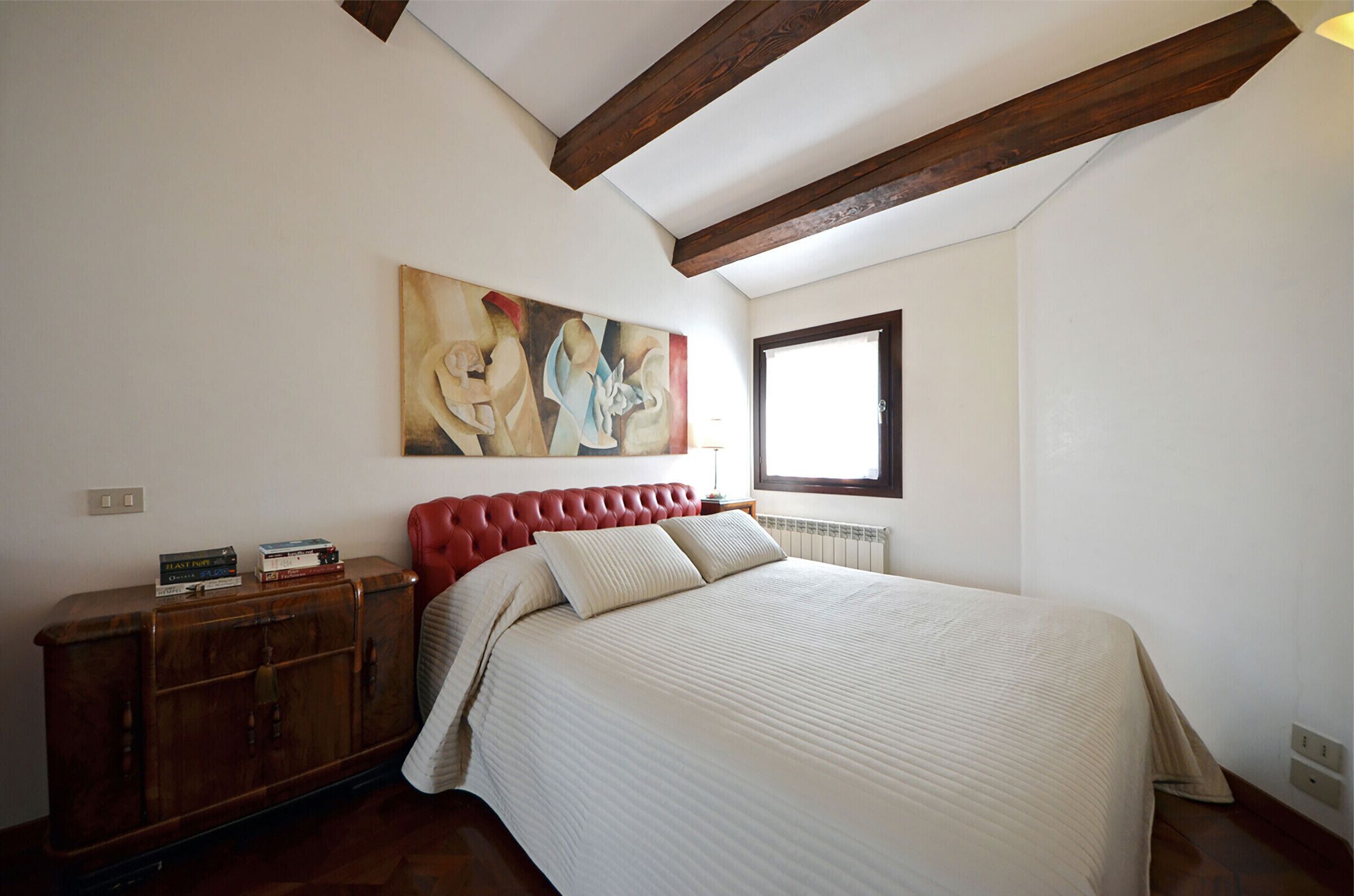 Een slaapkamer met een groot bed, een houten hoofdbord, een schilderij aan de muur en een raam.