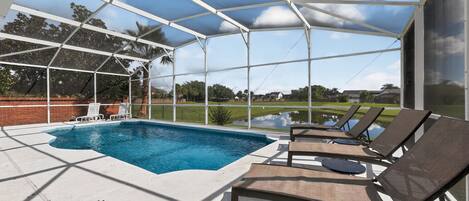 A covered outdoor swimming pool with lounge chairs and a view of a golf course.