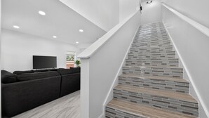 Ein modernes Wohnzimmer mit einem schwarzen Ecksofa, einem Flachbildfernseher und einer Treppe mit einem einzigartigen Fliesendesign.