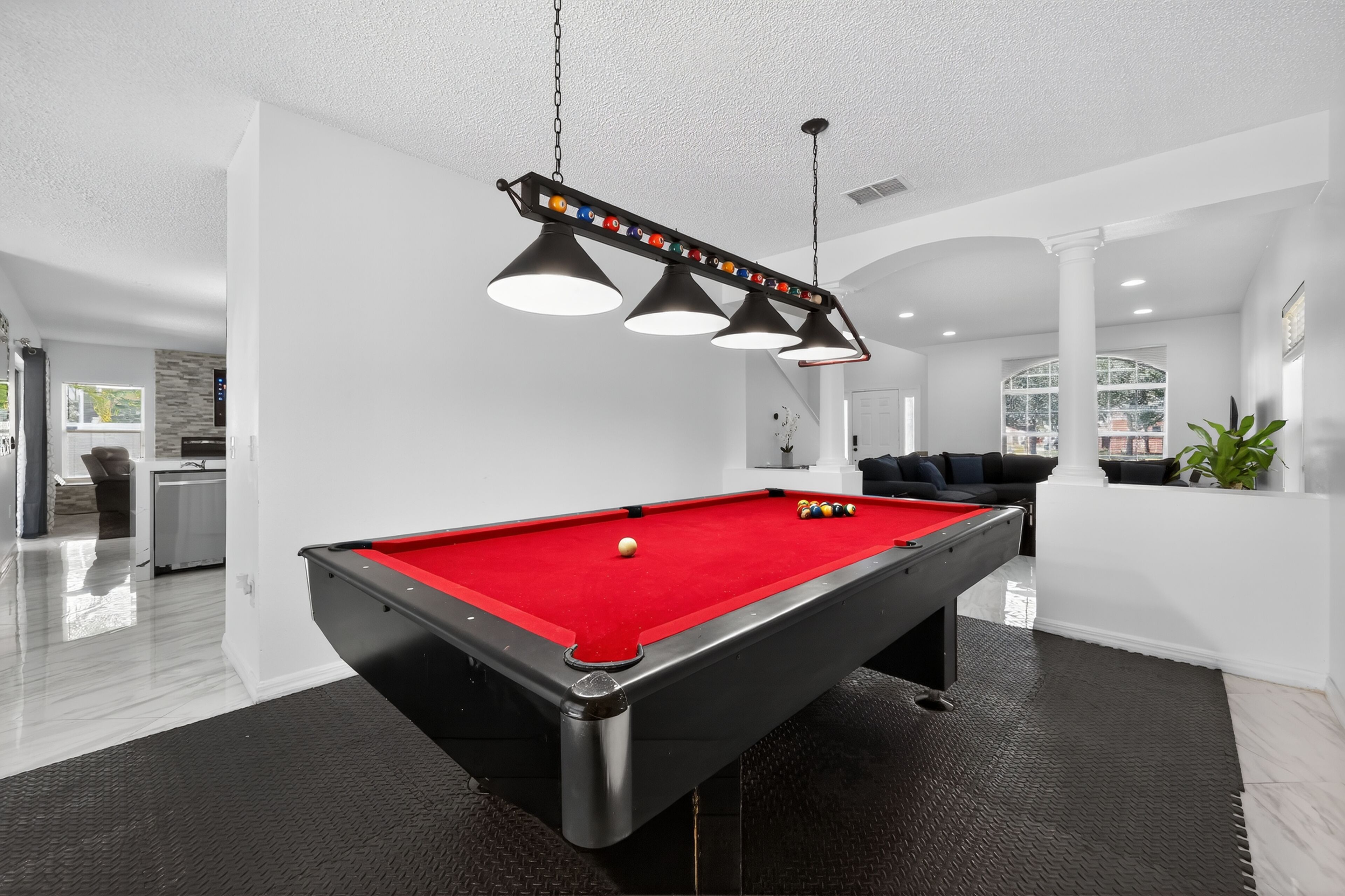 A pool table in a modern room with a red felt surface, black and white lighting fixtures, and a white ceiling.