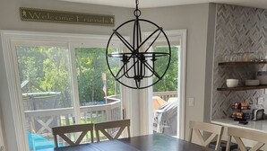 Un comedor con una mesa de madera oscura y sillas blancas, una lámpara colgante y vista a un patio de juegos a través de amplias ventanas.