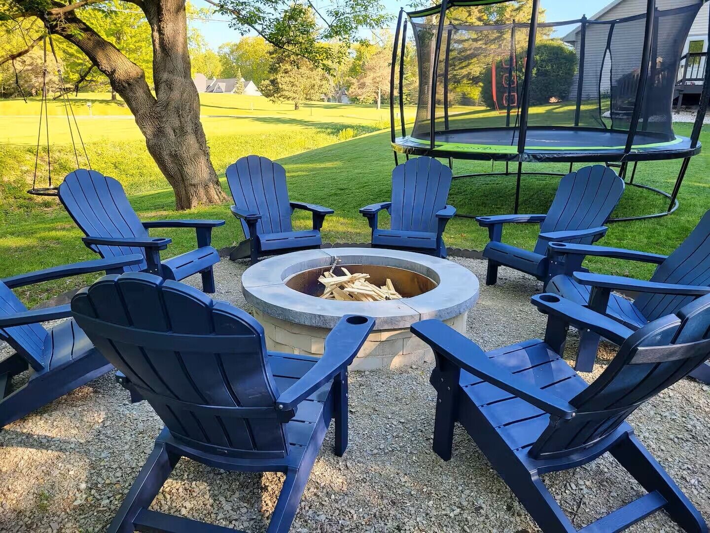 Un espacio circular con asientos y una chimenea rodeada por seis sillas tipo Adirondack.