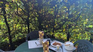 A round table with a green tablecloth, two white mugs with floral designs, a white teapot, a plate of biscuits, and a small glass jar.