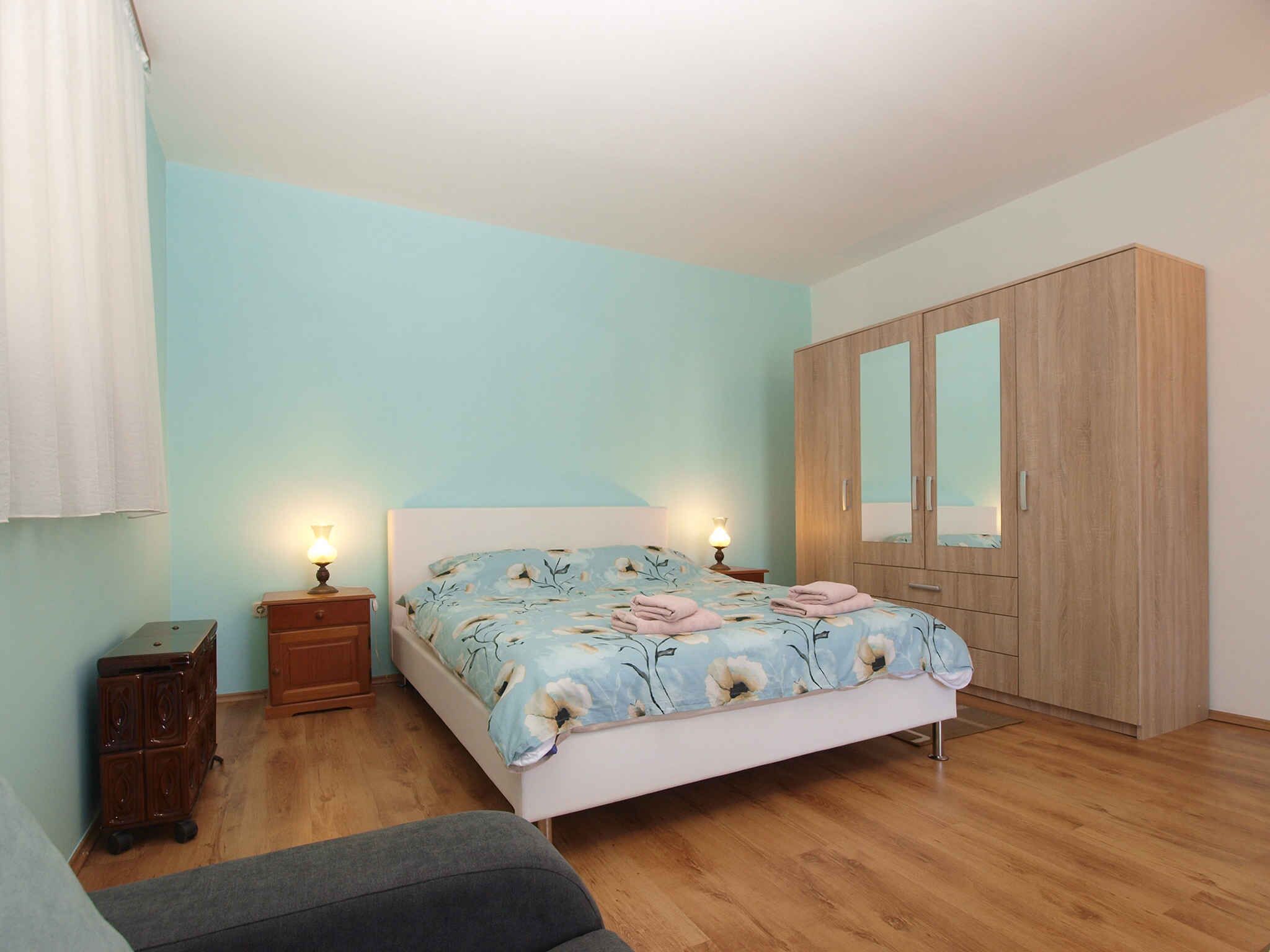 A bedroom with a bed, wooden wardrobe, bedside tables, and a small dresser.