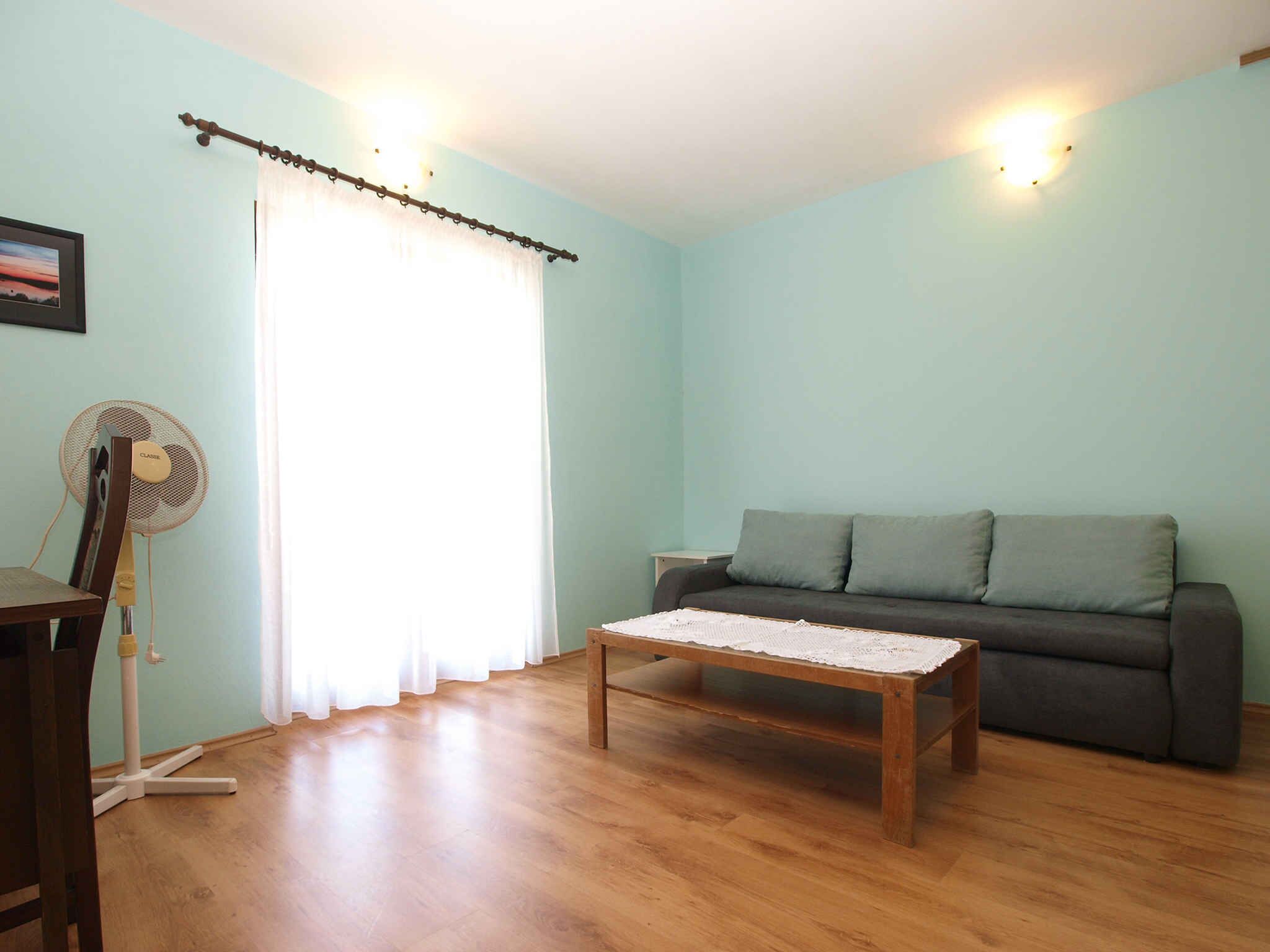A living room with a wooden floor, a grey sofa, a wooden coffee table, and a standing fan.
