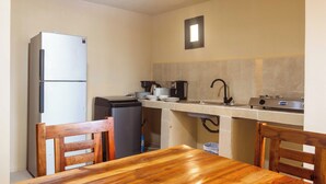 A compact kitchen with a refrigerator, stove, sink, and wooden dining table. - Roots inn  (Paje)