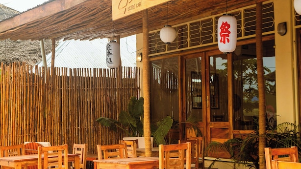A restaurant with outdoor seating, wooden chairs, and a bamboo fence. - Roots inn  (Paje)