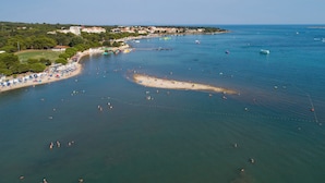 Vue aérienne d’une zone côtière avec une plage, des bateaux et des personnes qui se baignent.