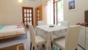 A room with a dining table, chairs, a bed, a TV, and a door leading outside.