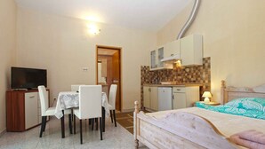 A compact hotel room with a bed, a small dining table with chairs, a kitchenette, and a television.