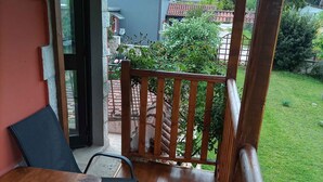 A wooden deck with a table and chairs, a glass door leading to a garden, and a view of a house with a red roof.