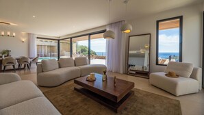 Un salon moderne doté d’un grand canapé d’angle, d’une table basse et offrant une vue sur l’océan grâce à de grandes fenêtres.