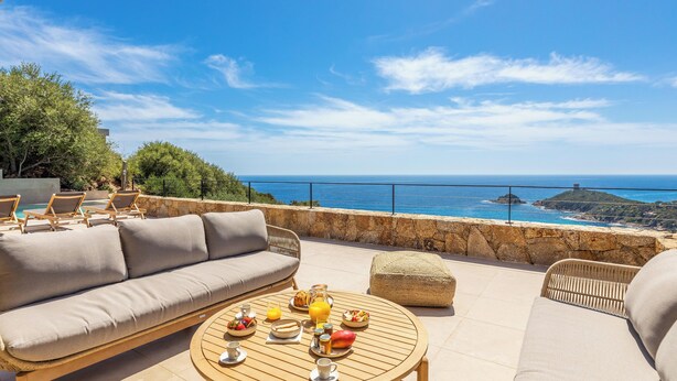 Une terrasse avec un canapé, des chaises et une table préparée pour le petit-déjeuner, le tout avec vue sur la mer.