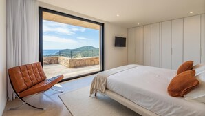 Une chambre moderne avec un grand lit, un fauteuil en cuir et un balcon offrant une vue panoramique.