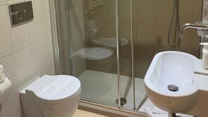 Moderni kylpyhuone, jossa on lasiseinällä varustettu suihku, kaksi valkoista pesuallasta ja wc.