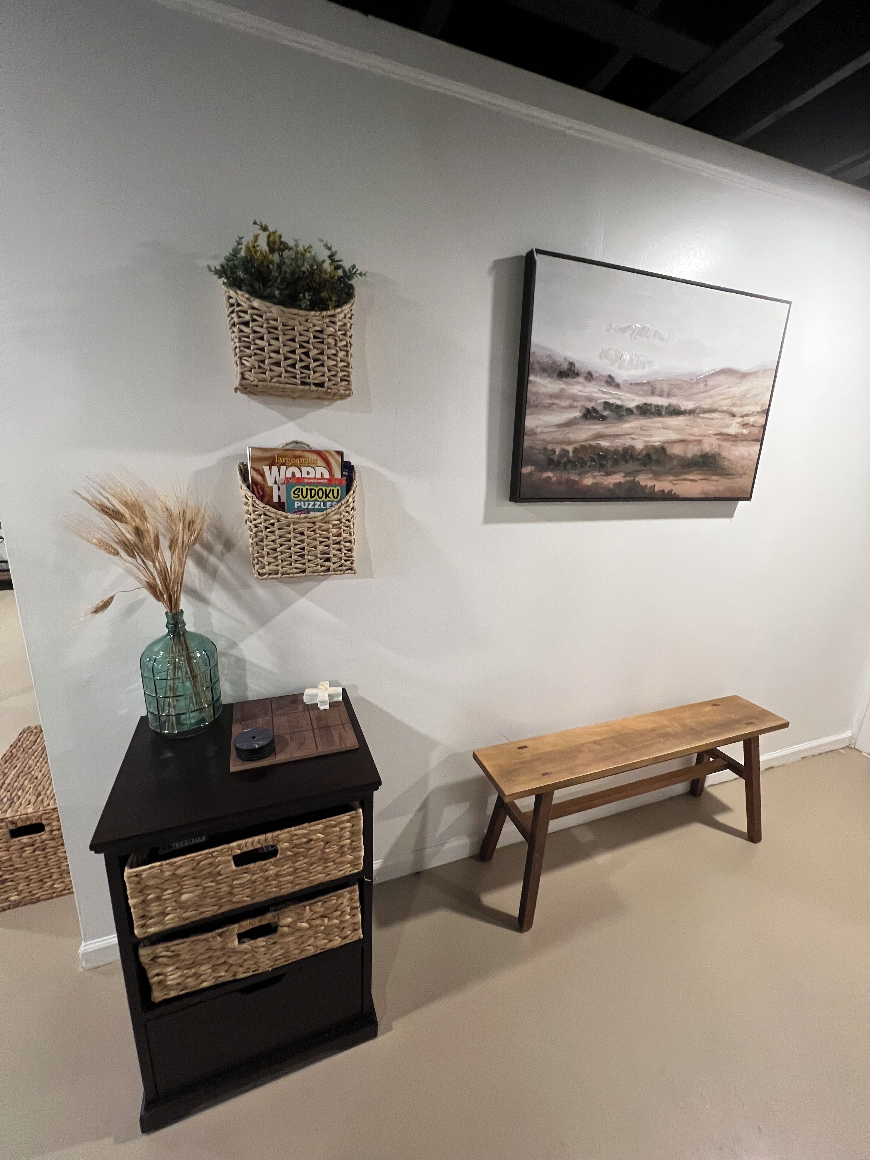 A room with a wooden bench, a black chest of drawers, and three wicker baskets on the wall.
