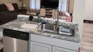 Una cocina compacta con lavavajillas, un lavamanos y un televisor al fondo.