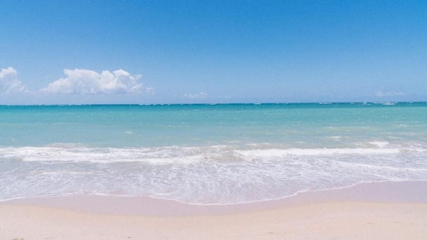 Une plage avec une eau d’un bleu limpide et un rivage sablonneux.