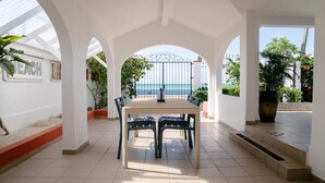 Un espace repas avec une table et des chaises, une vue sur la mer et un mur blanc orné d’une enseigne.