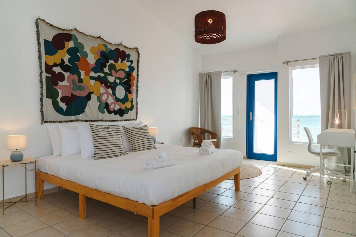 A bedroom with a large bed, a view of the sea, and a blue door.