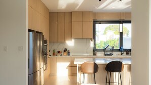 A modern kitchen with wooden cabinets, stainless steel appliances, and a large window providing natural light. - Outsite Puerto Rico Aguadilla - Work, Connect, Explore (Aguacate)