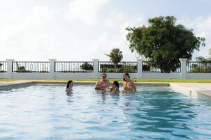 Una piscina con cerca blanca y un árbol grande al fondo.
