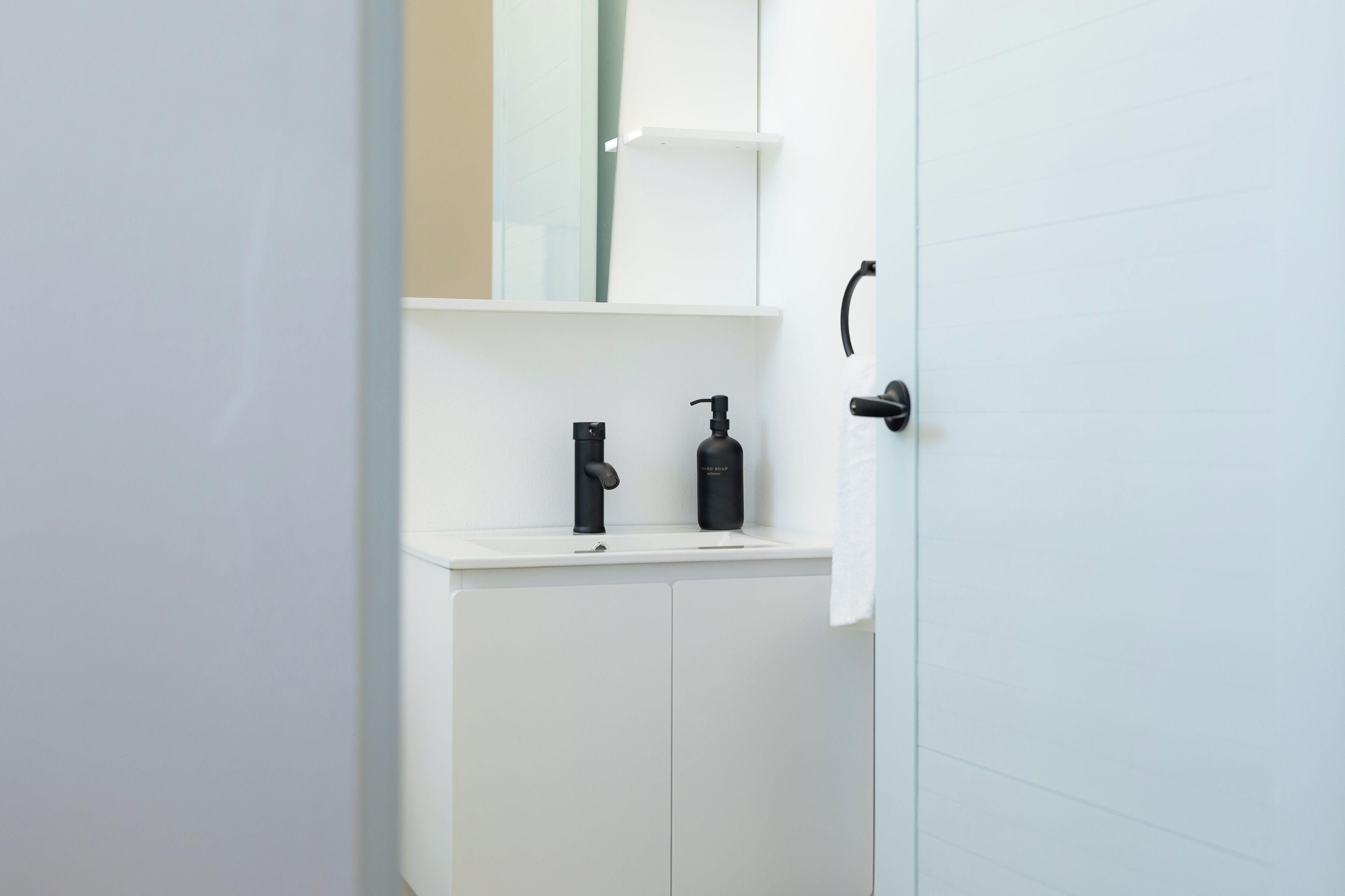 Une salle de bain blanche avec un lavabo blanc, un robinet noir et un distributeur de savon noir.