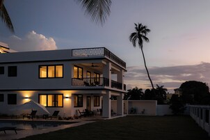 Una casa moderna de dos pisos con balcón, piscina e iluminación exterior al anochecer.