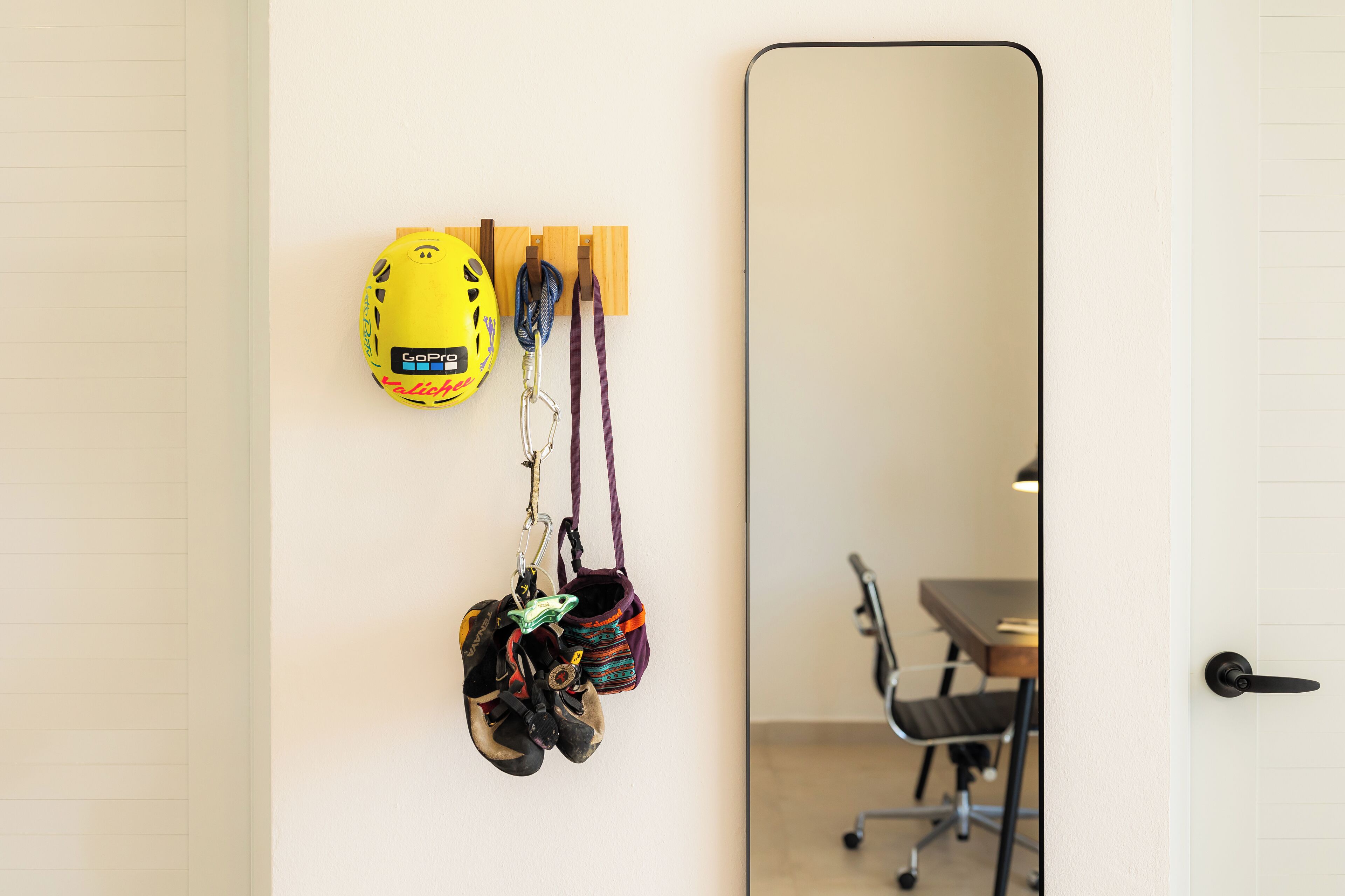 A room with a white door, a mirror, and a wall-mounted rack holding helmets and a GoPro camera.